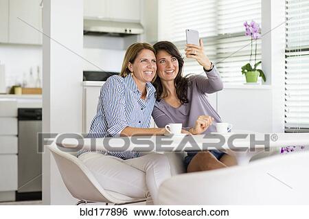 Stock Photograph - Caucasian women taking selfie in kitchen. Fotosearch