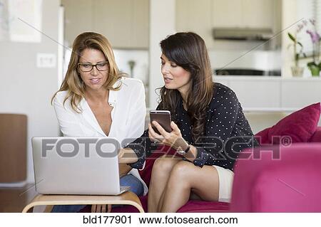 Stock Image - Caucasian women using cell phone on sofa. Fotosearch