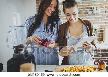 Stock Photo - Caucasian women using digital tablet in kitchen. Fotosearch