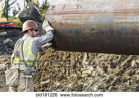 Stock Photograph - Caucasian worker hauling pipe at construction site. Fotosearch