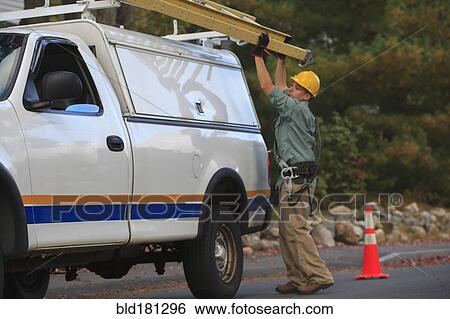 Stock Photograph - Caucasian worker loading ladder on truck. Fotosearch