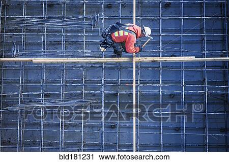 Stock Image - Caucasian worker nailing boards at construction site. Fotosearch