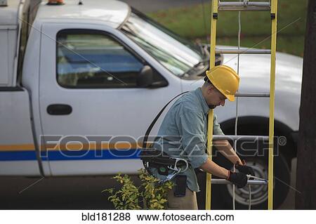 Stock Photo - Caucasian worker raising ladder outdoors. Fotosearch