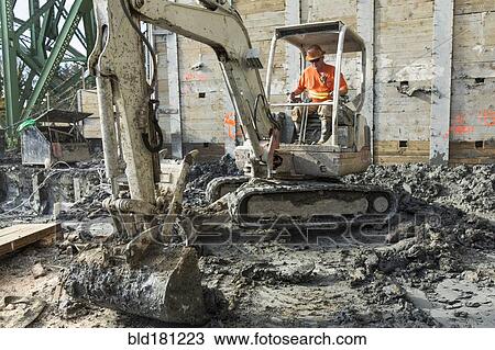 Stock Image - Caucasian worker using digger at construction site. Fotosearch