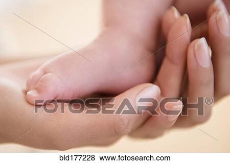 Stock Photo - Close up of mother holding bare foot of baby. Fotosearch