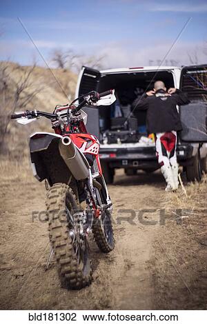 Stock Image - Close up of motorcycle behind dirt bike rider and van. Fotosearch
