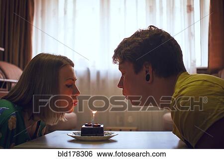 Stock Photograph - Couple blowing birthday candle on cupcake. Fotosearch