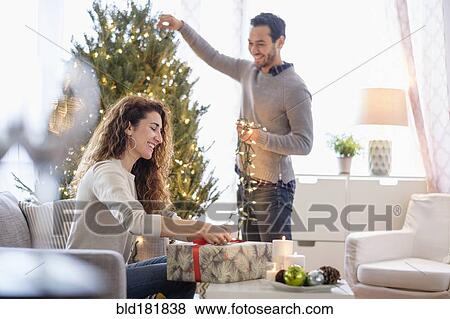 Couple decorating for Christmas in living room View Large Photo Image Stock Photo - Couple decorating for Christmas in living room. Fotosearch