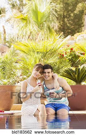 Stock Image - Couple drinking cocktails in swimming pool. Fotosearch