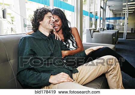 Stock Photo - Couple laughing on sofa. Fotosearch