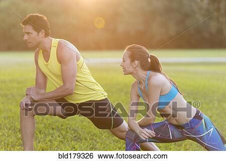 Stock Photograph - Couple stretching legs in field. Fotosearch