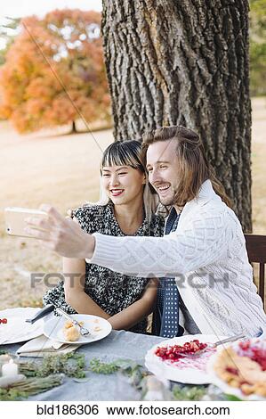 Stock Photograph - Couple taking selfie at outdoor table. Fotosearch