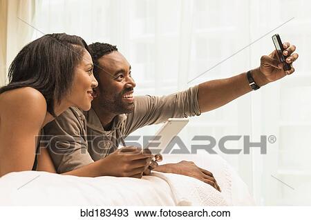 Stock Image - Couple taking selfie on bed. Fotosearch