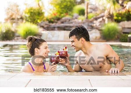 Stock Photography - Couple toasting with cocktails in swimming pool. Fotosearch