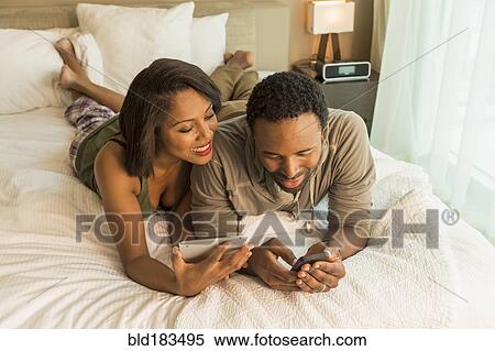 Stock Photography - Couple using digital tablet and cell phone on bed. Fotosearch