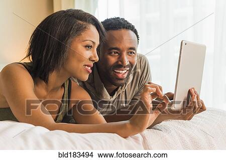 Picture - Couple using digital tablet on bed. Fotosearch