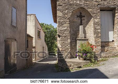 Stock Image - Crucifix shrine in wall alcove on village sidewalk. Fotosearch
