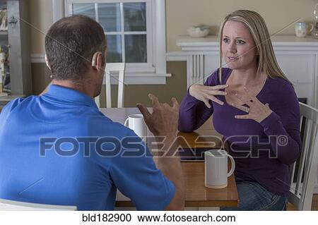Stock Image - Deaf Caucasian couple signing at dinner table. Fotosearch
