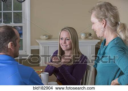 Picture - Deaf Caucasian friends signing at dinner table. Fotosearch