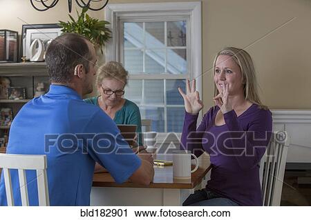 Stock Image - Deaf Caucasian friends signing at dinner table. Fotosearch