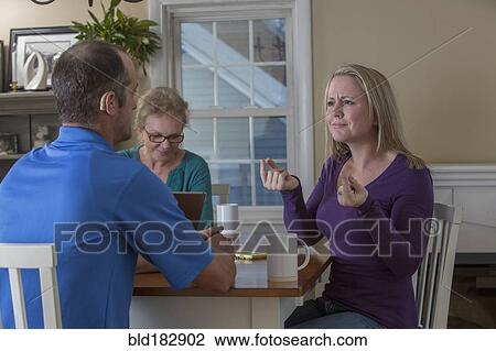 Stock Image - Deaf Caucasian friends signing at dinner table. Fotosearch