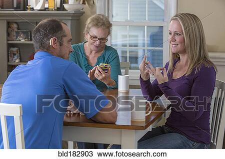 Stock Image - Deaf Caucasian friends signing at dinner table. Fotosearch