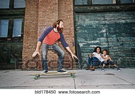 Stock Image - Family riding skateboards on sidewalk. Fotosearch