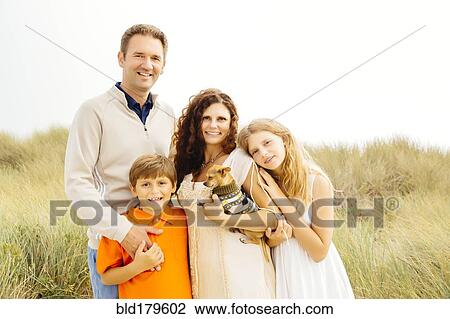 Stock Image - Family smiling with dog on beach. Fotosearch