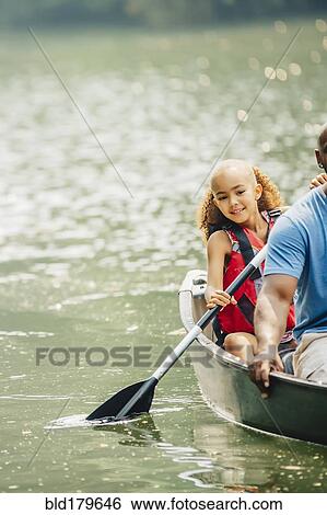 Stock Photograph - Father and daughter rowing canoe in lake. Fotosearch