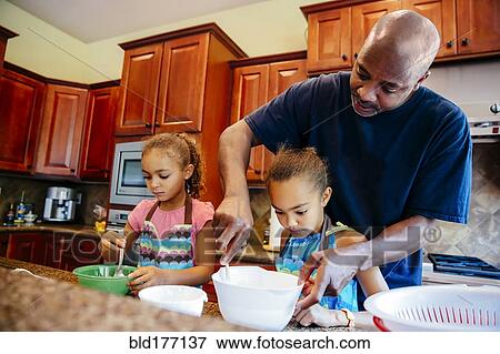 Stock Photo - Father and daughters cooking in kitchen. Fotosearch