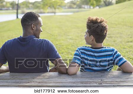 Father and son sitting at table in park View Large Photo Image Stock Image - Father and son sitting at table in park. Fotosearch