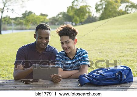 Stock Image - Father and son using digital tablet in park. Fotosearch