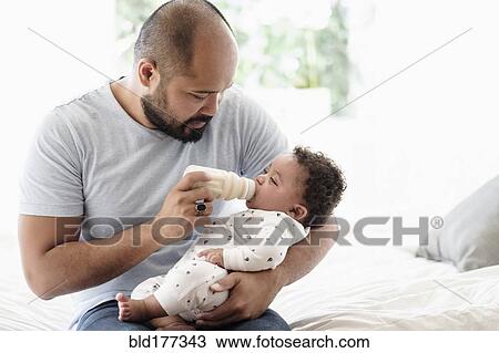 Stock Image - Father bottle feeding baby son. Fotosearch
