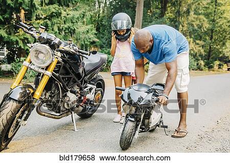 Stock Photo - Father helping daughter with miniature motorcycle. Fotosearch