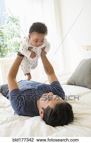 Stock Image - Father holding baby son on bed. Fotosearch