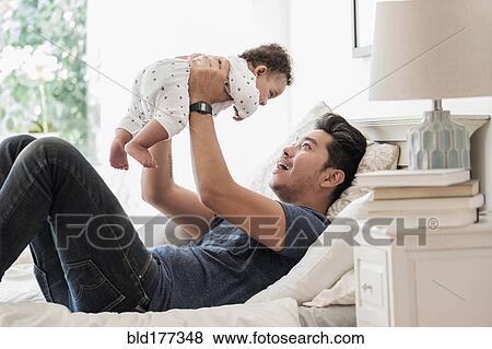 Stock Photo - Father holding baby son on bed. Fotosearch