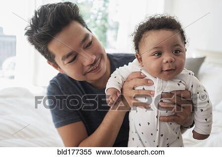 Father holding baby son on bed View Large Photo Image Stock Photography - Father holding baby son on bed. Fotosearch