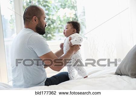 Stock Image - Father playing with baby son on bed. Fotosearch