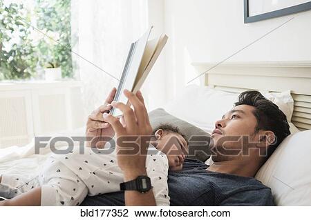 Stock Image - Father reading with sleeping baby son. Fotosearch