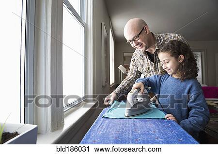 Stock Image - Father teaching daughter to iron fabric. Fotosearch