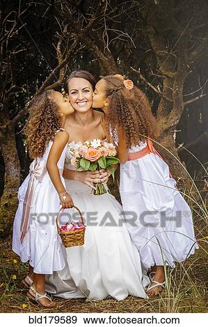 Stock Photo - Flower girls kissing bride outdoors. Fotosearch
