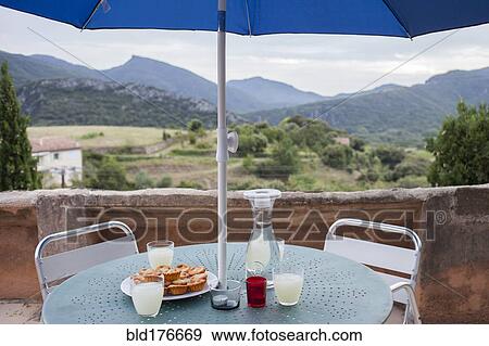 Stock Photo - Food and drinks on balcony table over rural landscape. Fotosearch