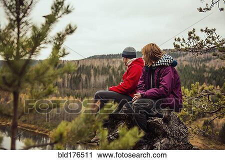Stock Image - Friends sitting on rock on remote hillside. Fotosearch