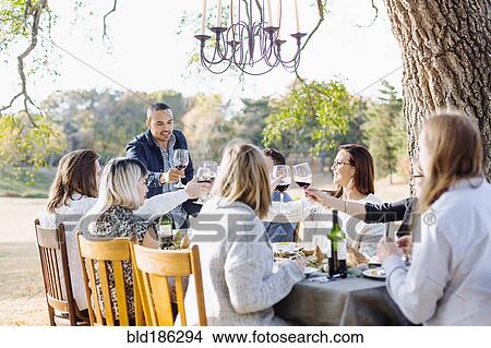 Picture - Friends toasting with wine at outdoor table. Fotosearch