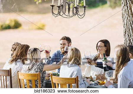 Stock Image - Friends toasting with wine at outdoor table. Fotosearch