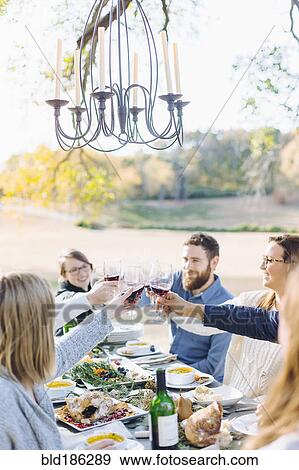Stock Photo - Friends toasting with wine at outdoor table. Fotosearch