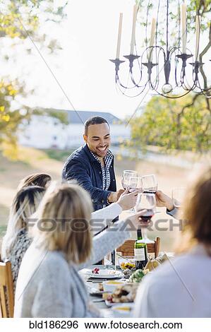 Friends toasting with wine at outdoor table View Large Photo Image Stock Photograph - Friends toasting with wine at outdoor table. Fotosearch