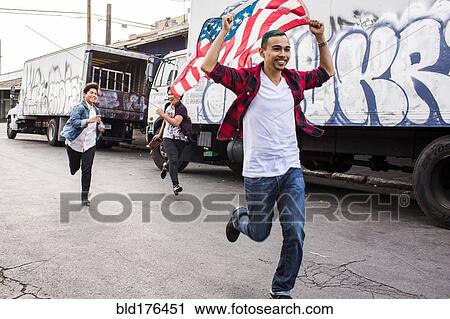 Stock Image - Friends waving American flag outdoors. Fotosearch