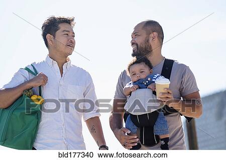 Stock Image - Gay fathers doing errands with baby son. Fotosearch