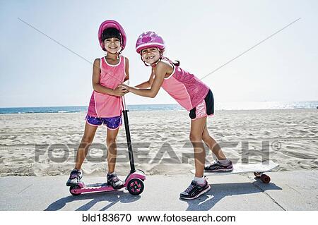 Stock Image - Girls playing on skateboard at scooter at beach. Fotosearch